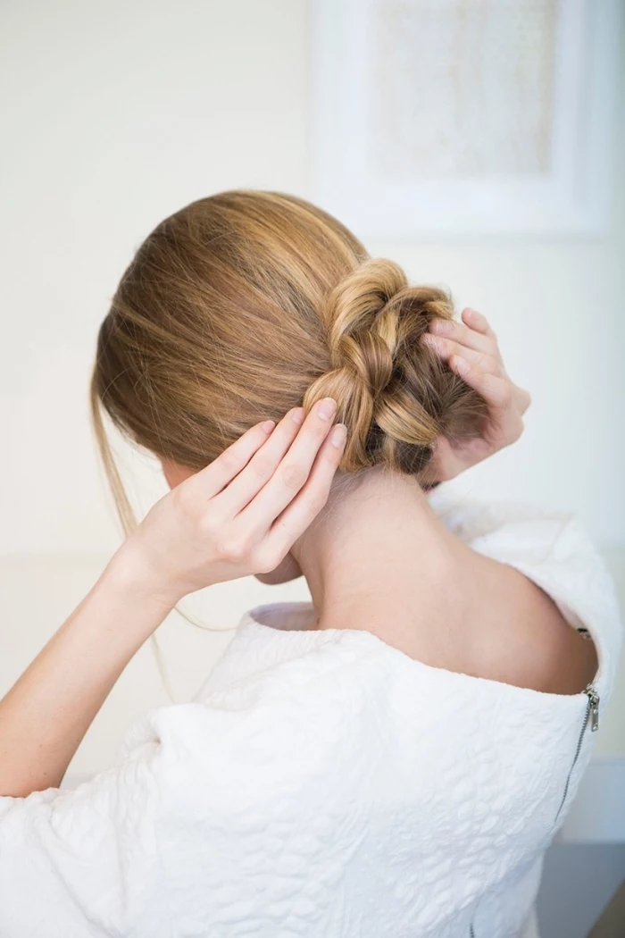 woman wearing a white top, blonde hair, in a braided bun, low updo, woman fixing her hair, beautiful hairstyles
