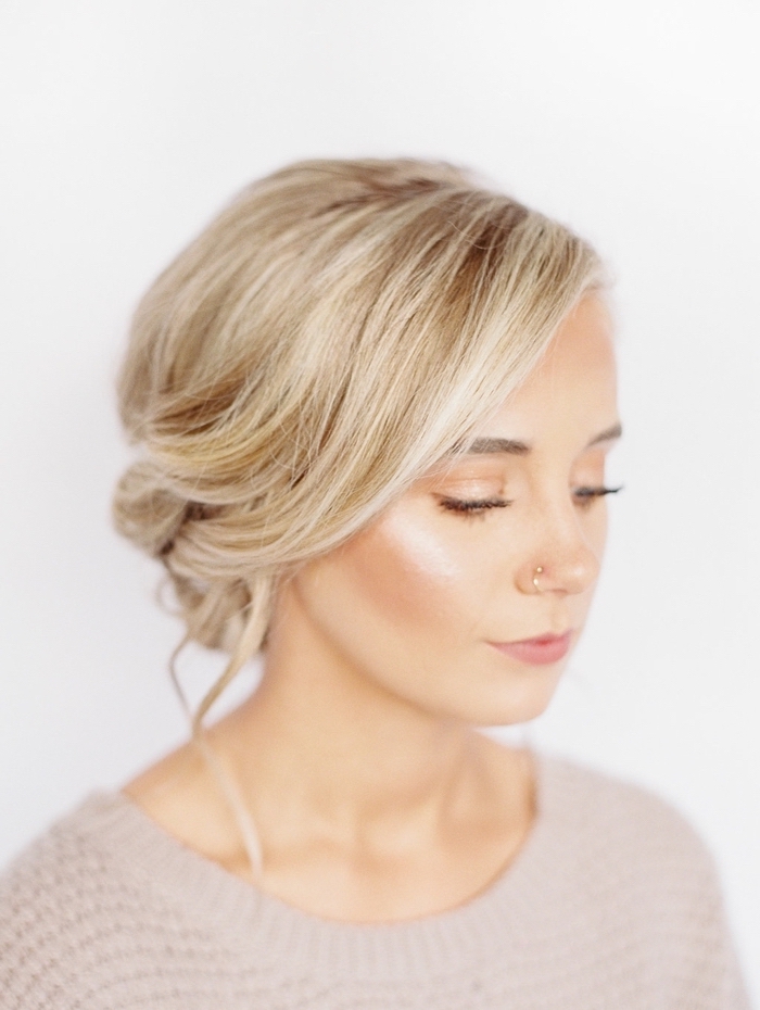 blonde hair, in a low updo, updos for long hair, woman wearing a nose earring, and a grey sweater
