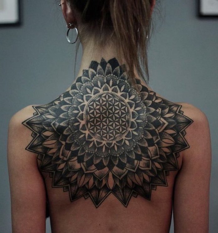 back tattoo, blonde hair, mandala flower tattoo, grey background, silver earrings