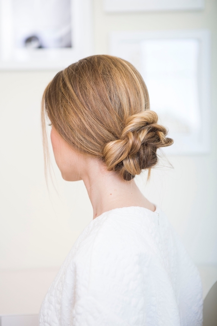 beautiful hairstyles, blonde hair, in a low braided bun, woman wearing a white top, in front of a white background
