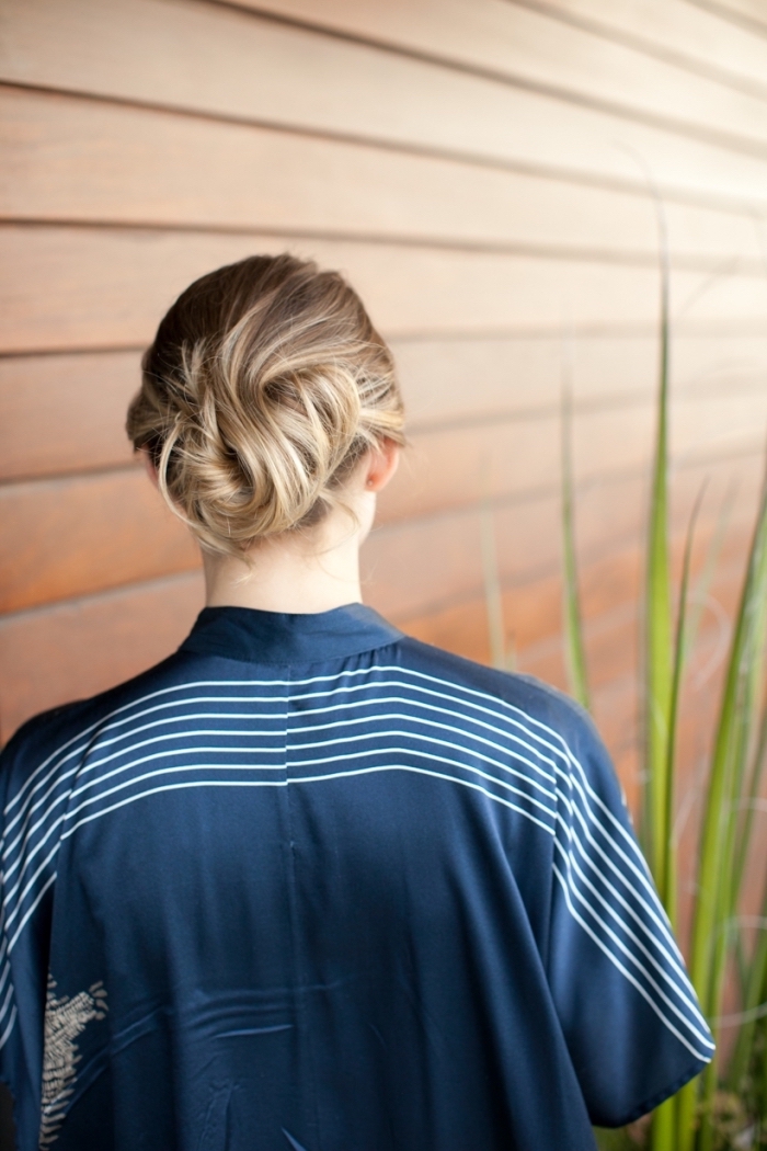 woman wearing a blue satin shirt, dark blonde hair, with highlights, in a low updo, braid hairstyles for long hair