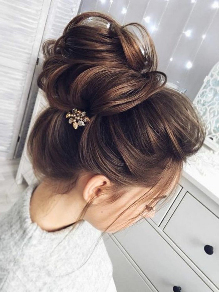brown hair with highlights, in a high messy updo, floral hair accessory, braids for long hair, grey sweater