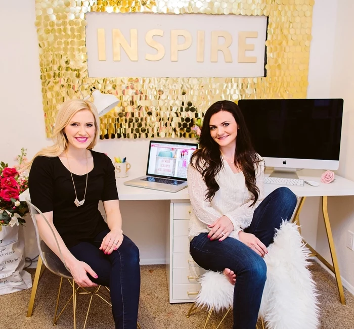 two women sitting, in front of a gold sequinned frame, inspire quote, hanging over a white desk, home wall decor