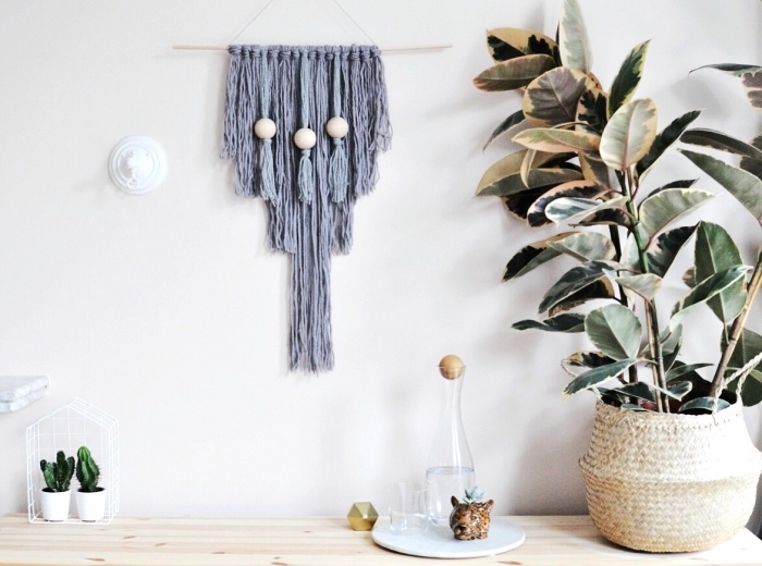 grey macrame wall art, hanging on a white wall, white wall decor, large potted plant on the side, over a wooden table