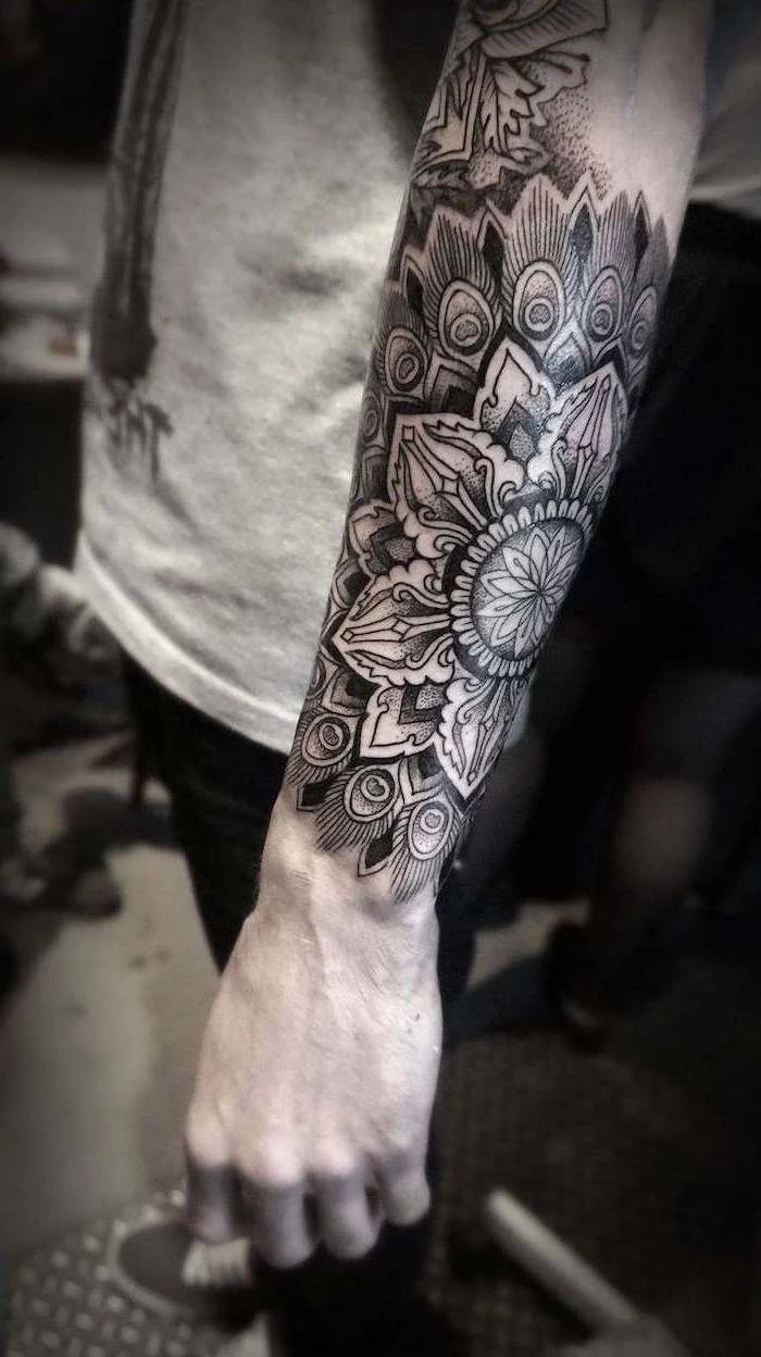 forearm tattoo, man wearing, grey top, black jeans, mandala symbols