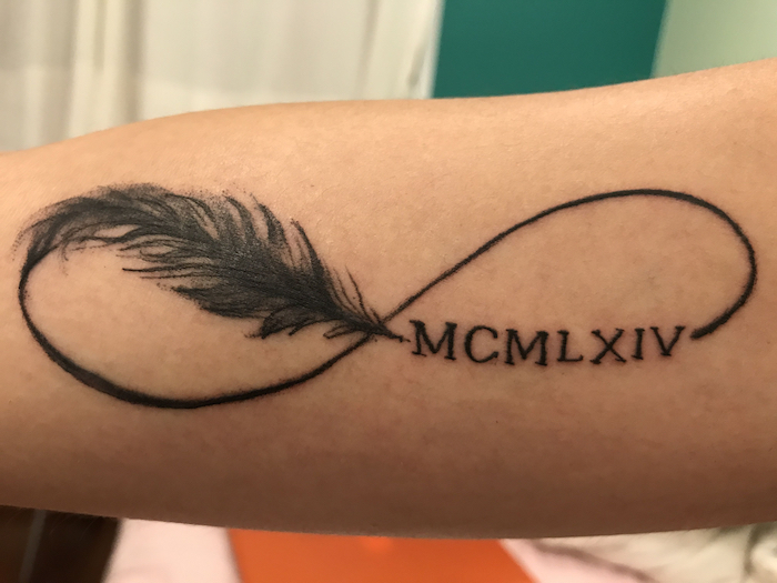 infinity symbol, with a feather, forearm tattoo, side arm tattoos, white and blue background, meaningful roman numeral tattoos