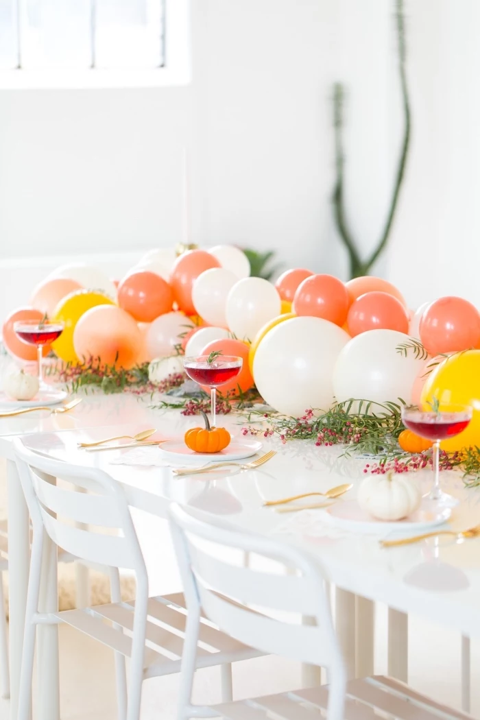 centerpiece ideas, orange white and yellow balloons, table runner, white table, wine glasses, orange white pumpkins