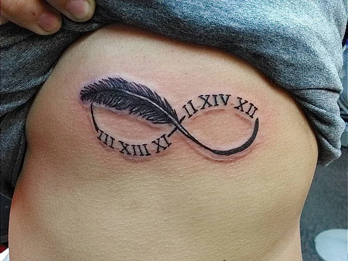 rib cage tattoo, infinity symbol, with feather, grey blouse, roman numeral date tattoo