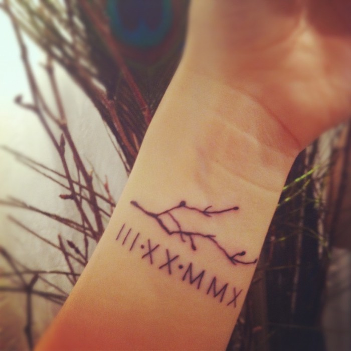 tree branch, wrist tattoo, roman numerals tattoo on chest, tree branches in the background