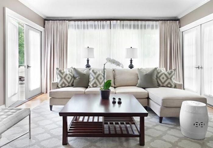 white corner sofa, wooden table, small living room furniture arrangement, tall windows, printed carpet
