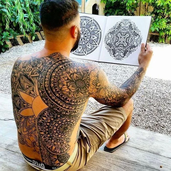whole back tattoo, sleeve tattoo, man sitting on wooden steps, holding a sketchbook, small mandala tattoo