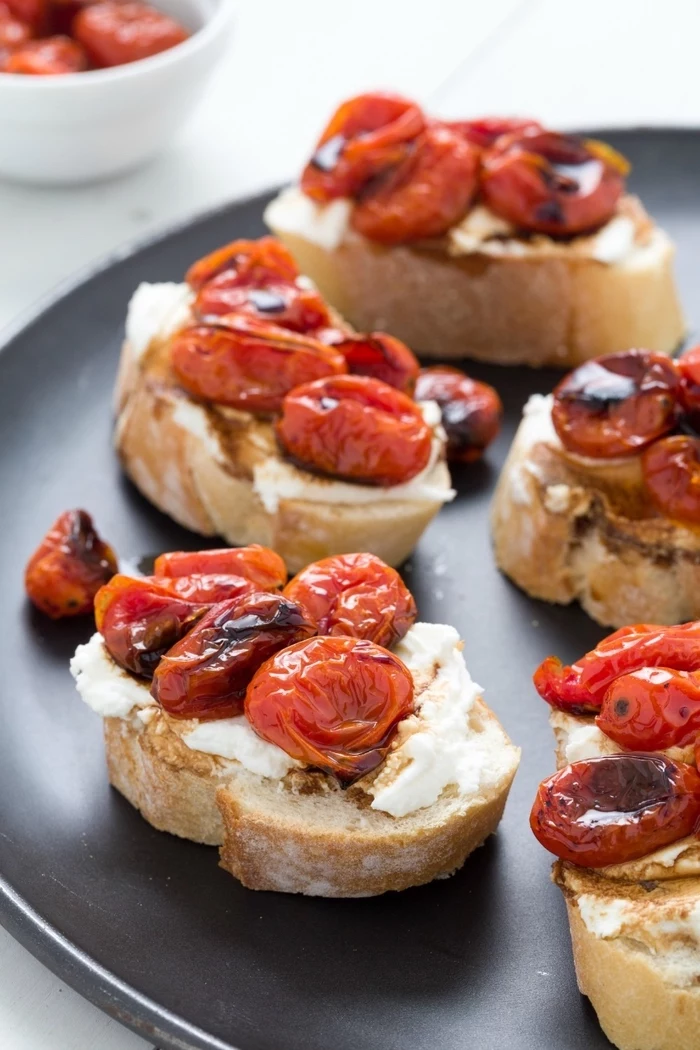 bread slices, baked cherry tomatoes on top, cream cheese, vegan hors d oeuvres, black plate