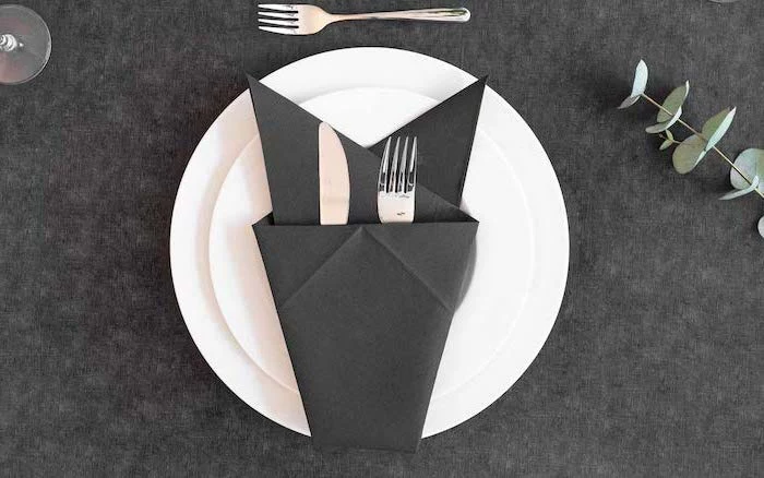 thanksgiving napkin folding, black napkin, silverware inside, on white plates, on a black table cloth