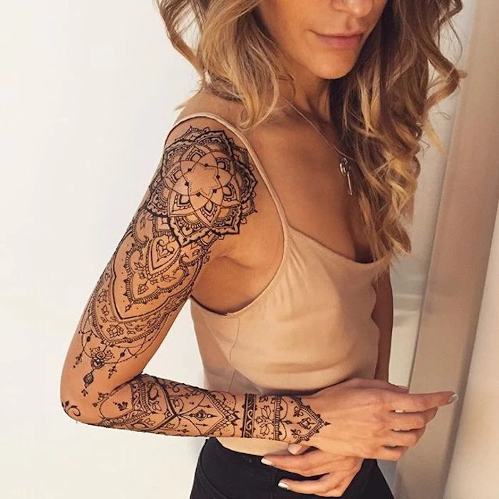 mandala flower tattoo, arm sleeve tattoo, small tattoos for girls, beige top, black pants, blonde hair