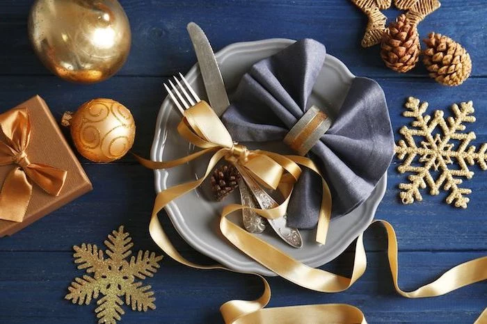 blue napkin with ring, napkin folding, golden ribbon, on a grey plate, with silverware, christmas ornaments
