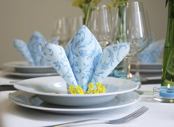blue napkin, yellow flowers, in a white plate, easy napkin folding, wine glasses around