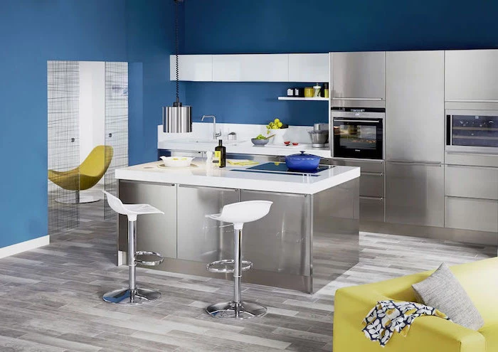 yellow sofa, blue walls, small kitchen island with seating, white bar stools, metal kitchen island and cabinets