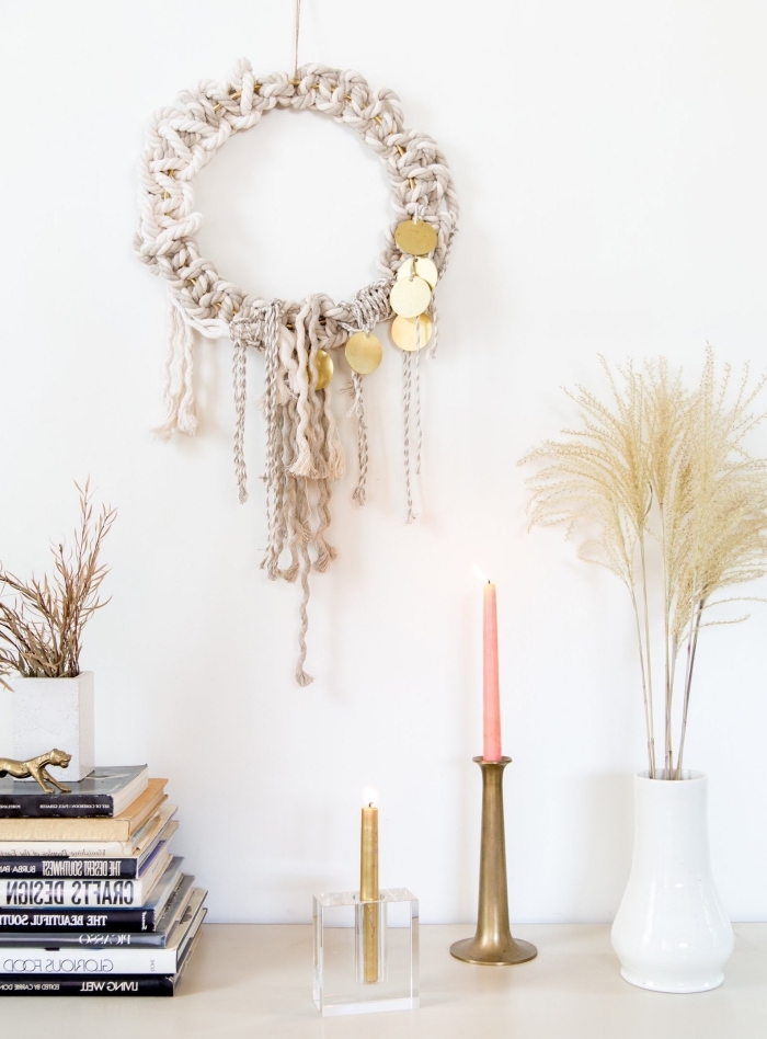 white wall, white ceramic vase, large macrame wall hanging, stack of books, pink and cold candles