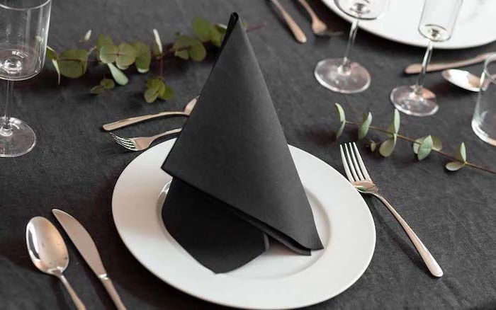 black folded napkin, on a white plate, silverware arranged around it, easy napkin folding