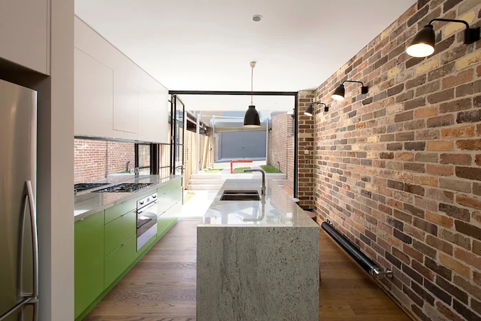 brick wall, green cabinets and drawers, granite countertop, small kitchen island with seating, wooden floor