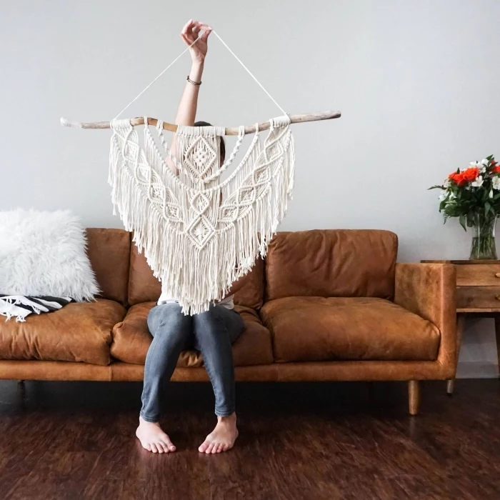 large macrame wall hanging, brown velvet sofa, woman sitting on it, wooden floor, white wall