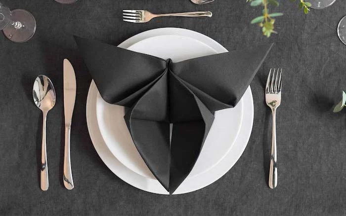 napkin folding, butterfly shaped, black napkin, on a white plate, arranged silverware around