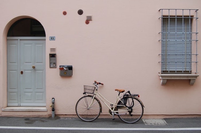bycicle-in-front-of-house-white-door-pink-wall-pastel-pink-background bicycle standing in front of a pink wall, pink background tumblr, white door