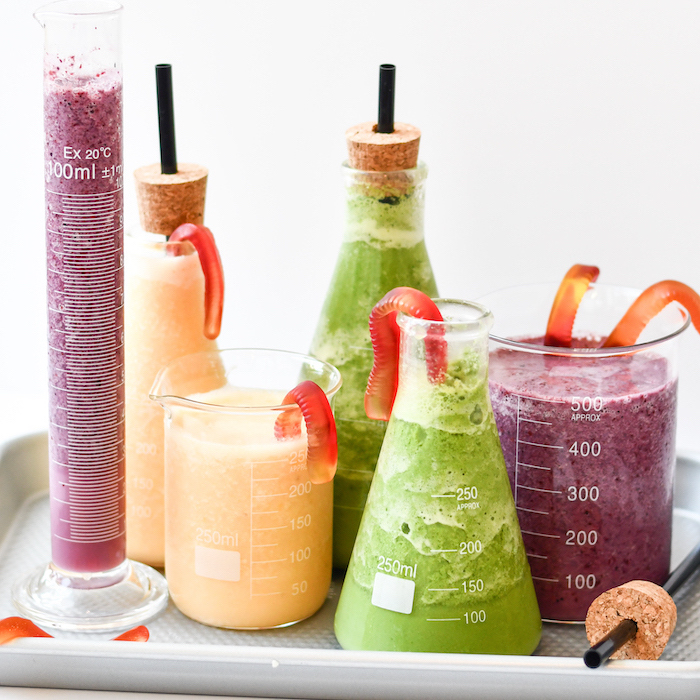 chemistry bottles, filled with smoothies, corks with black straws, smoothie recipes, on white tray