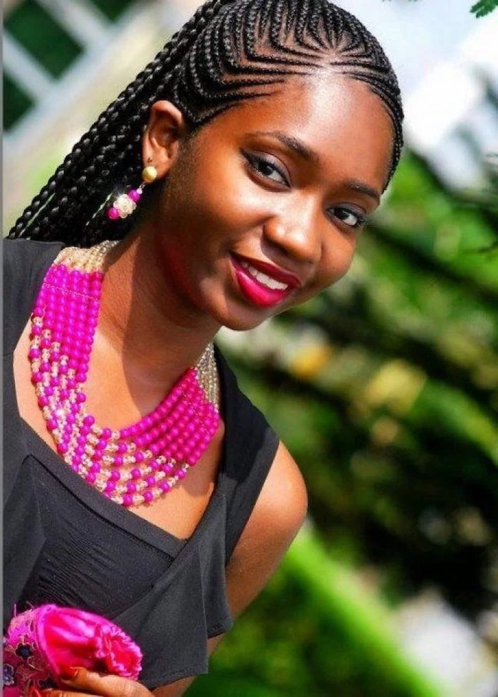 girl smiling, wearing a black top, pink jewellery, with black hair, big cornrows hairstyles