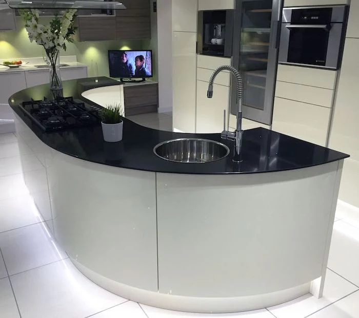 curved kitchen island, island countertop, white tiled floor, white cabinets, black countertop