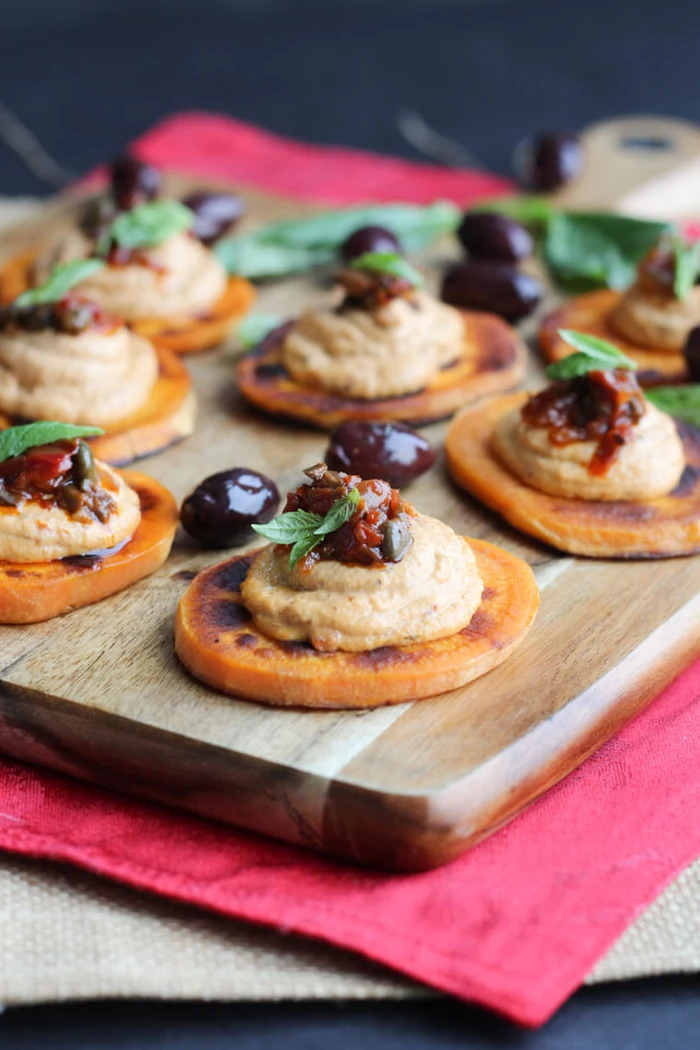 sweet potato slices, hummus and olives on top, veggie appetizers, arranged on a wooden board