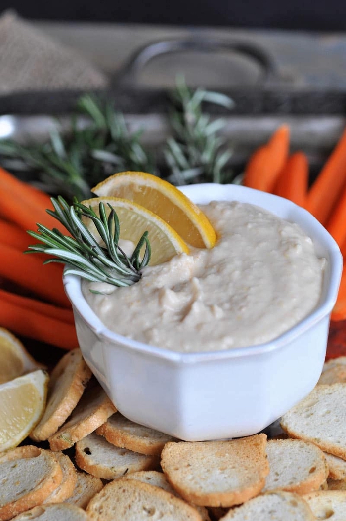 hummus in a white bowl, with lemon and rosemary, easy vegan appetizers, baked bruschetta