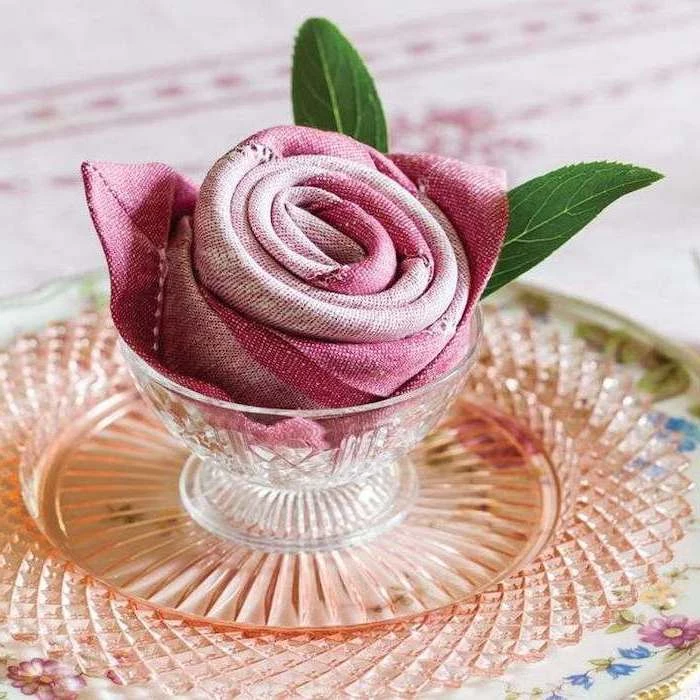 pink napkin, in the shape of a rose, inside a glass bowl, napkin folding, floral plate
