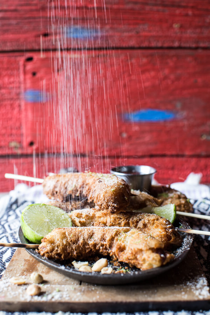 fried bananas, veggie appetizers, sliced lime, covered in powder sugar, on a wooden board