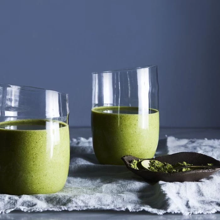 two glasses, with green smoothies inside, how to make a fruit smoothie, blue background