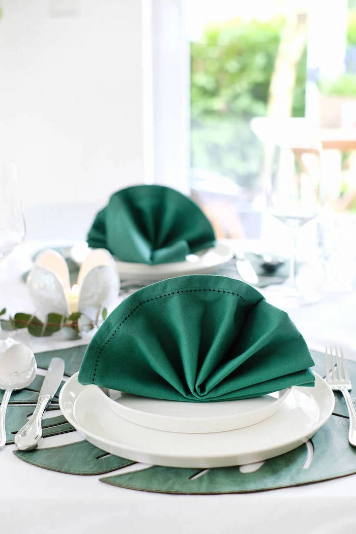 green napkins, in the shape of a fan, on white plates, paper napkin folding, silverware around it