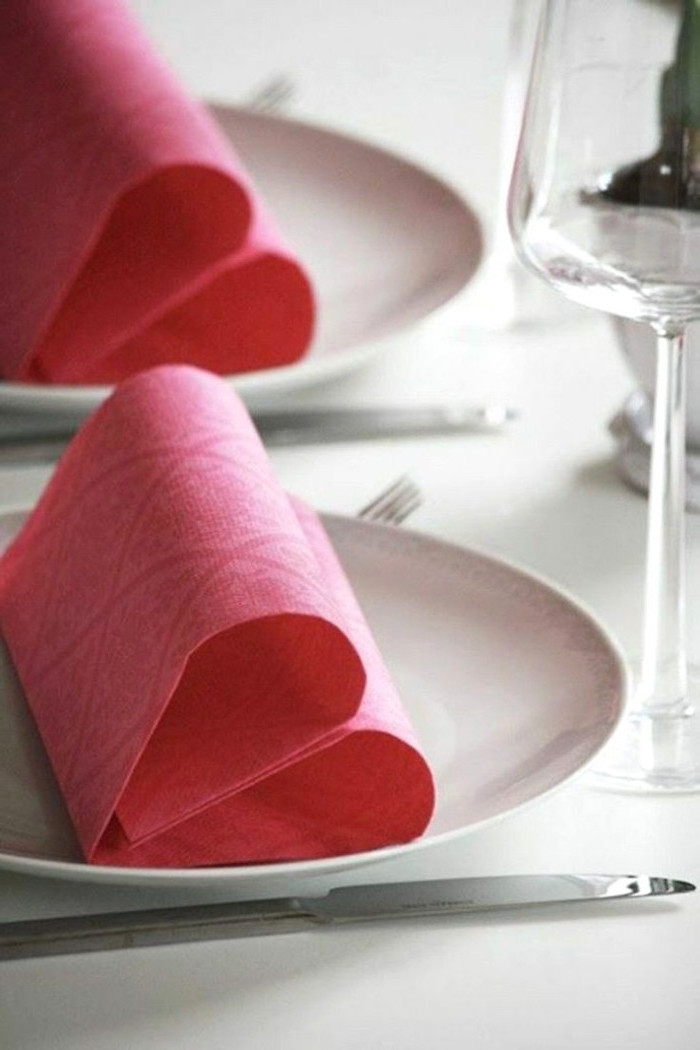 fancy napkin folding, pink napkins, in the shape of hearts, on white plates, wine glasses