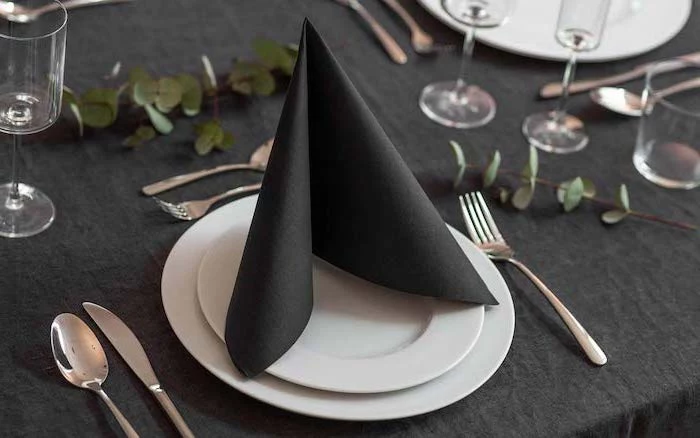 black folded napkin, on white plates, silverware arranged around them, napkin folding with rings