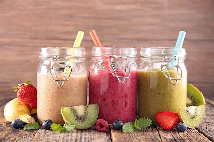 three jars, filled with different smoothies, healthy smoothie recipes, scattered fruit slices around