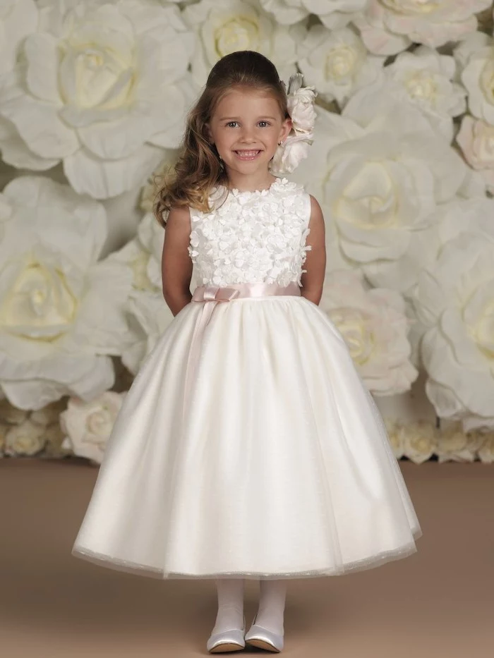 white roses background, white lace and tulle dress, white shoes, flower girl hair, brown wavy hair