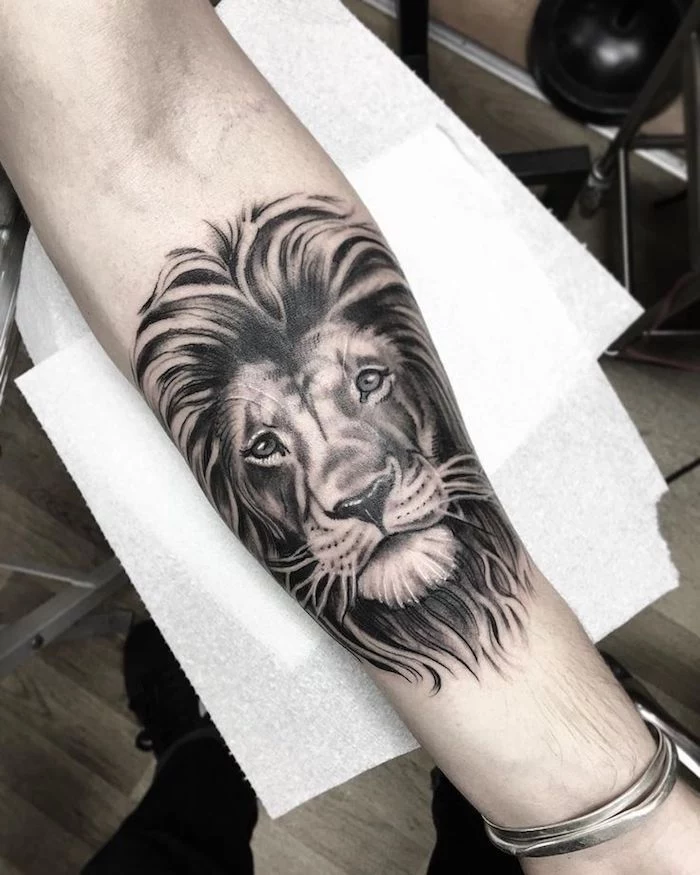 lion head, hand on white paper, silver bracelet, forearm sleeve tattoo