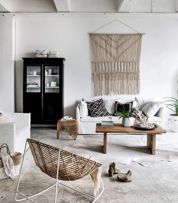 white sofa, macrame wall art, black cabinet, wooden table, cement floor, wooden armchair