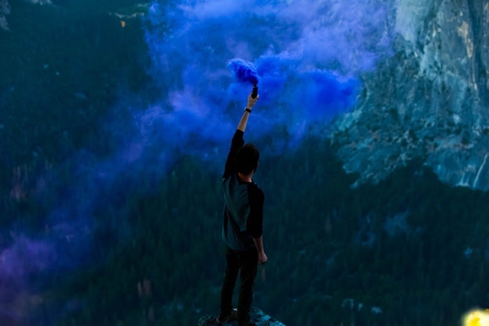 man holding a blue bomb, standing on top of a rock, background tumblr, mountain landscape