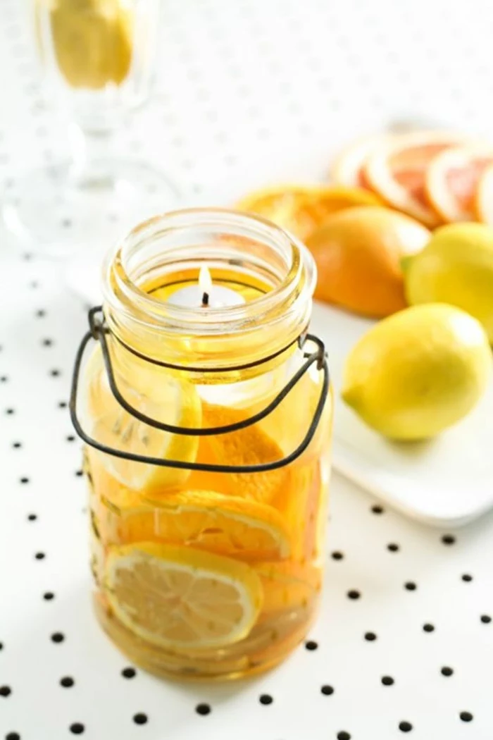 large mason jar, lemon slices inside, filled with water, how to make candle wax, citrus fruits, on a white plate