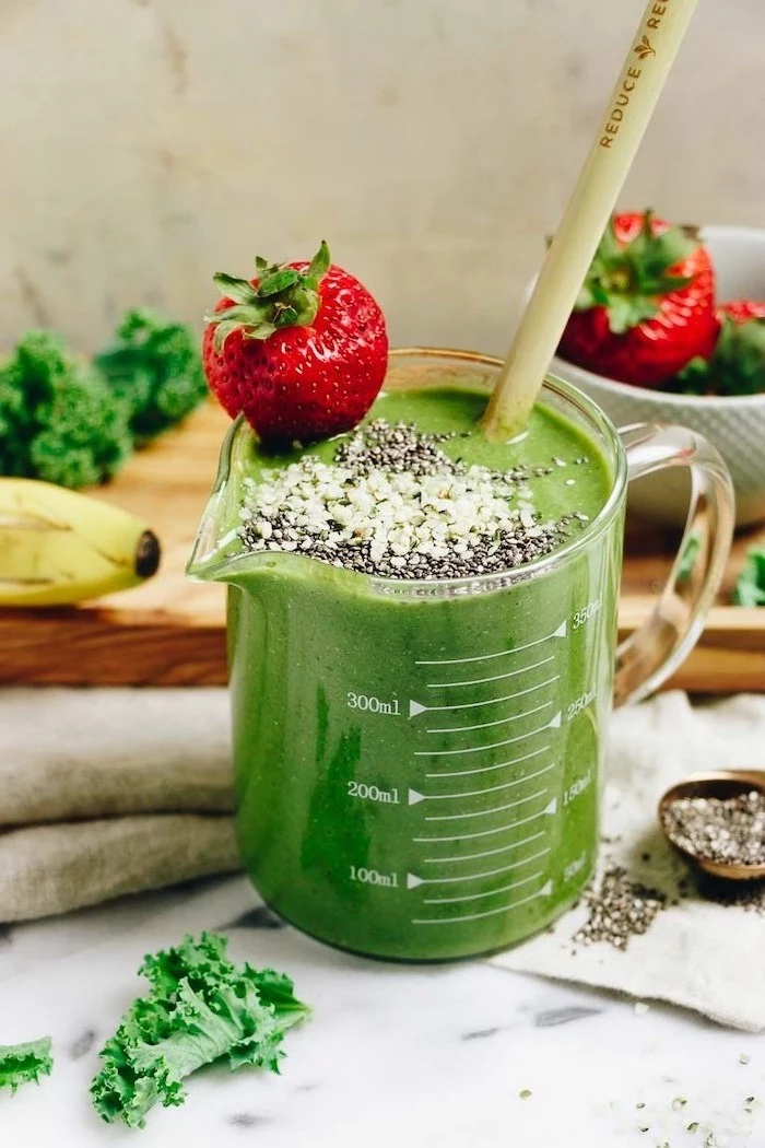 green smoothie, in a measuring cup, smoothie recipes with frozen fruit, strawberry on the rim