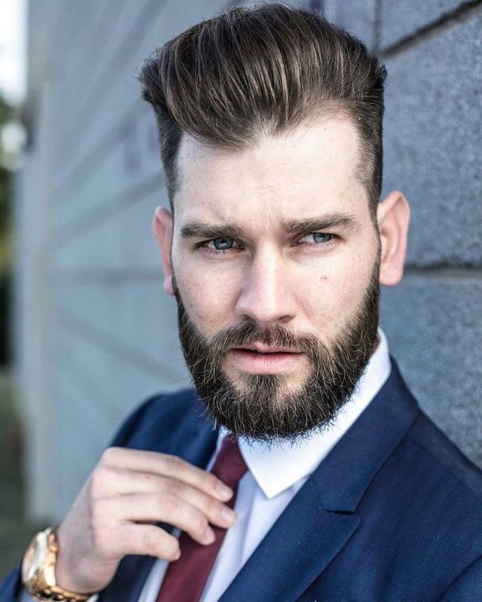 navy suit, white shirt, red burgundy tie, medium haircuts for men, brick wall, gold watch, brown hair and beard
