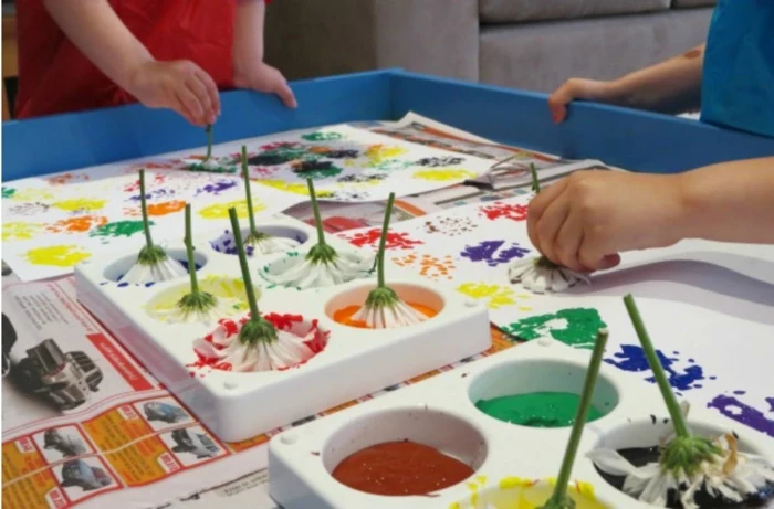 children painting with flowers, hands on activities, orange and red, yellow and purple paint