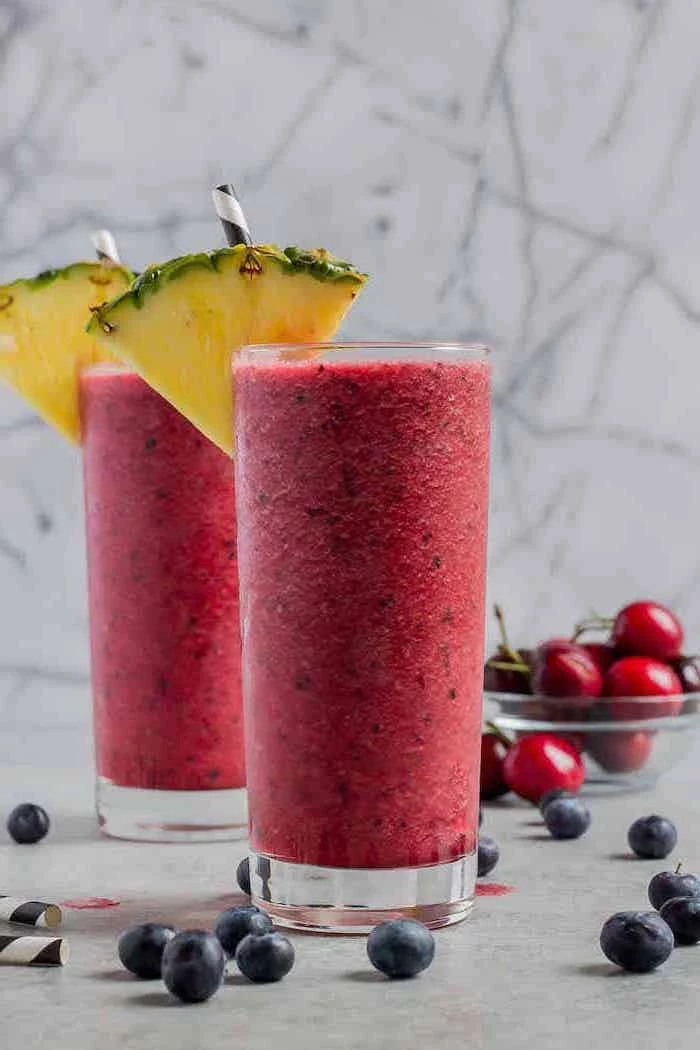 tall glasses, pineapple slices on the rim, how to make healthy smoothies, blackberries around, cherries in a bowl