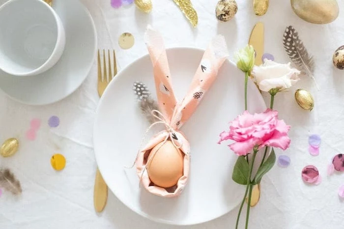 bunny shaped napkin, egg inside it, on a white plate, how to fold cloth napkins, pink and white flowers