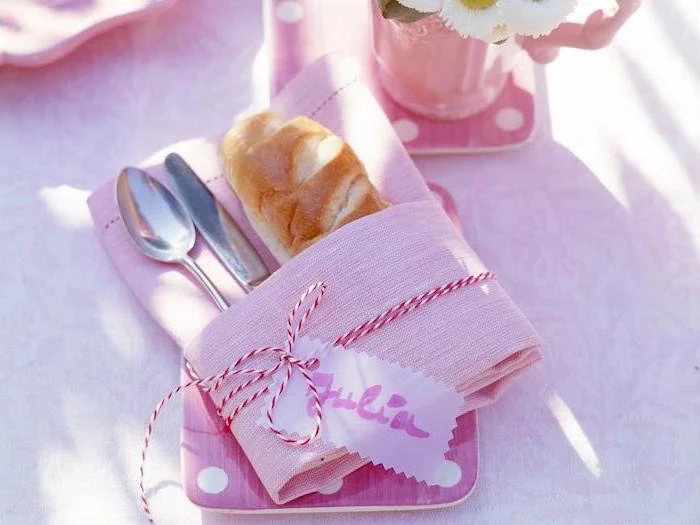 pink napkin, silverware and bread inside, red and white ribbon around it, name tag, how to fold napkins